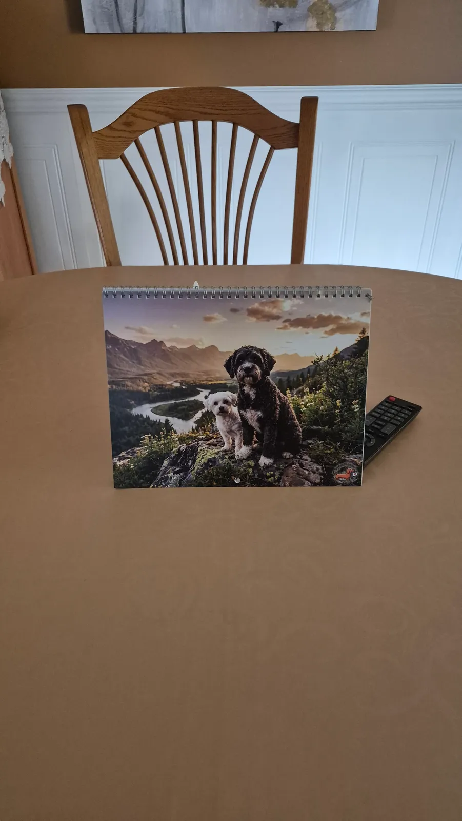 Un calendrier Nature imprimé illustrant deux chiens dans un paysage de montagne repose sur une table.