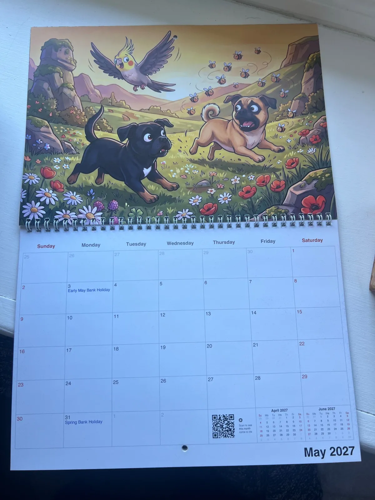 A printed Funny Cartoon calendar showing two dogs and a bird running through a field on a desk.