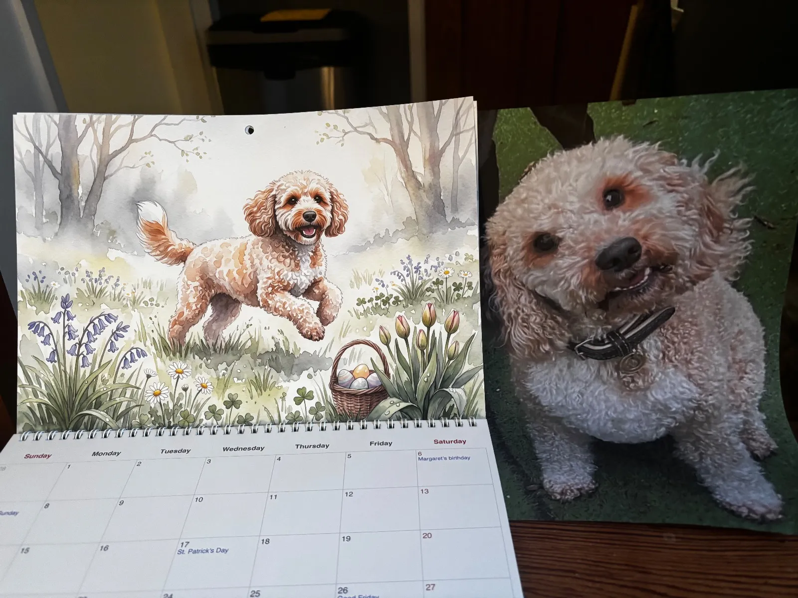 A printed Watercolor calendar opened to a spring illustration sits next to a photo of the dog.