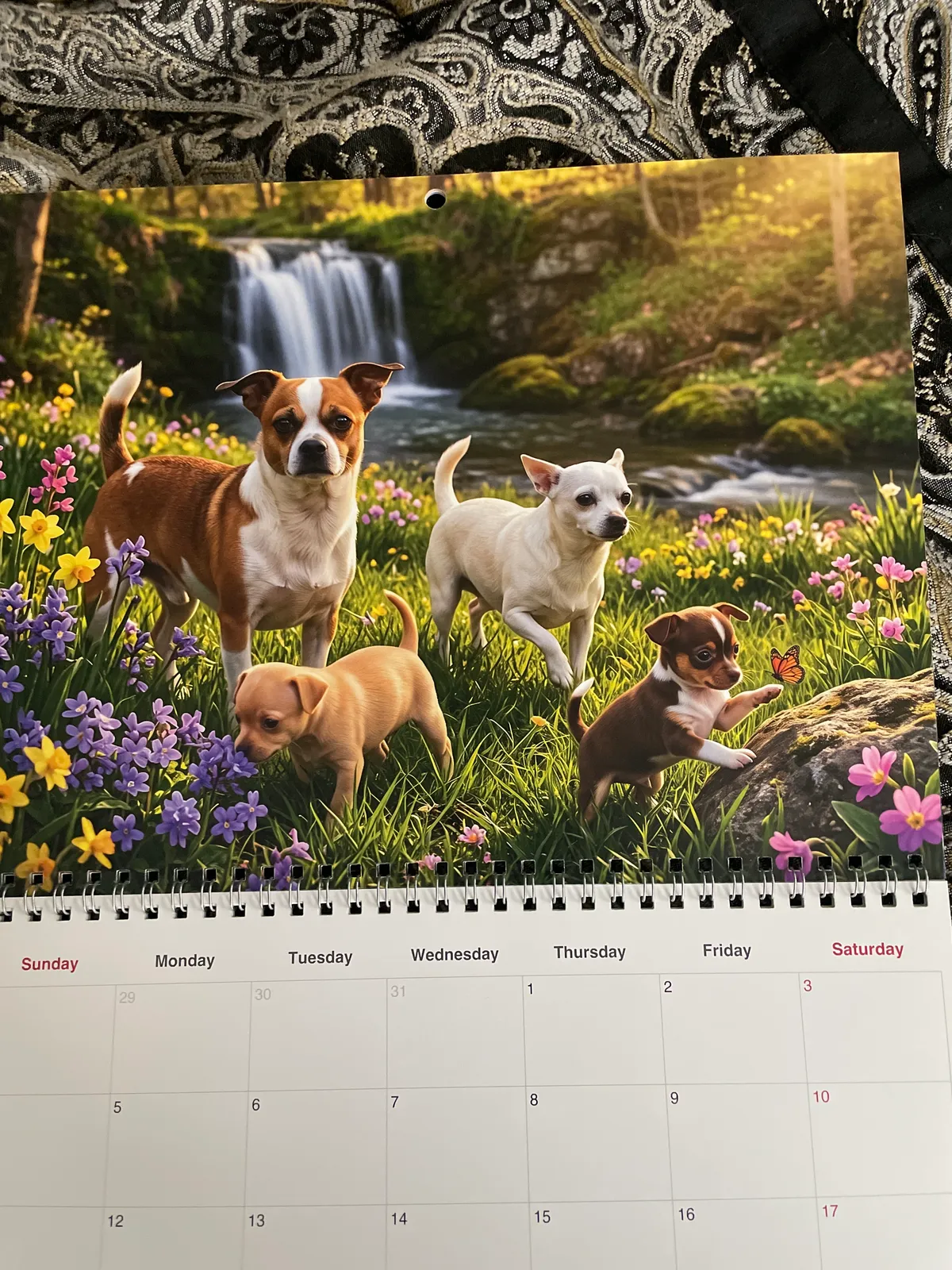 Un calendrier imprimé montre quatre chiens dans une prairie fleurie près d’une chute d’eau.