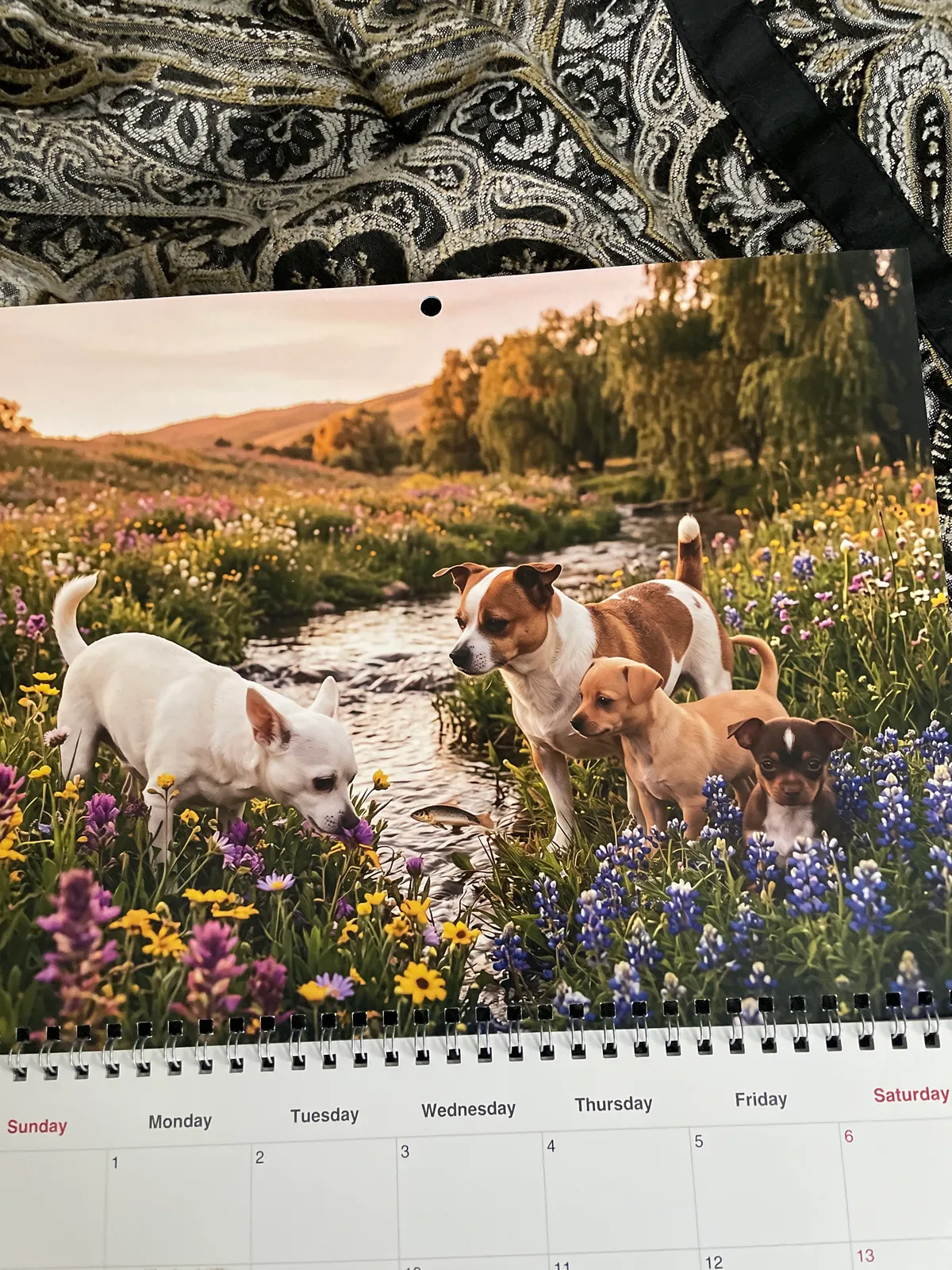 Un calendrier imprimé montre quatre chiens rassemblés au bord d’un ruisseau parmi des fleurs sauvages.
